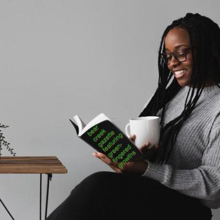 A woman sitting in a chair reading and enjoying an issue of Bear Creek Gazette featuring Greenfingered Growths by James C. Holland